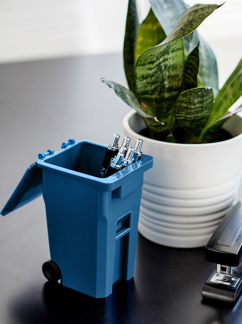 blue promotional mini recycling cart holding pens on an office desk beside a plant and stapler
