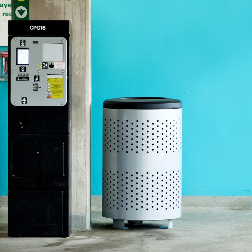 durable powder coated steel waste bin in a parking garage beside the pay station