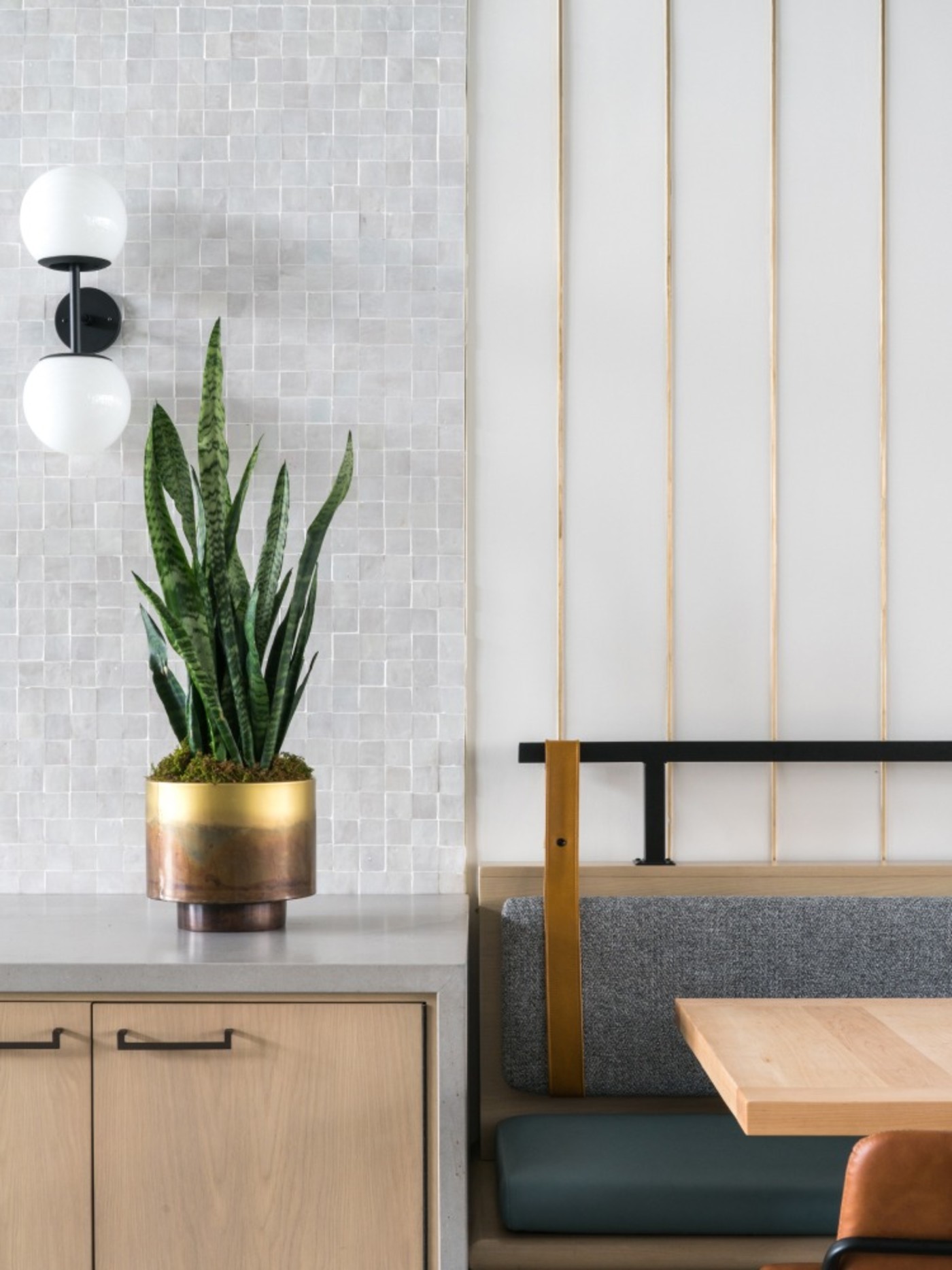 a room with white tiled walls, a cabinet with a potted plant and an upholstered bench and coffee table.