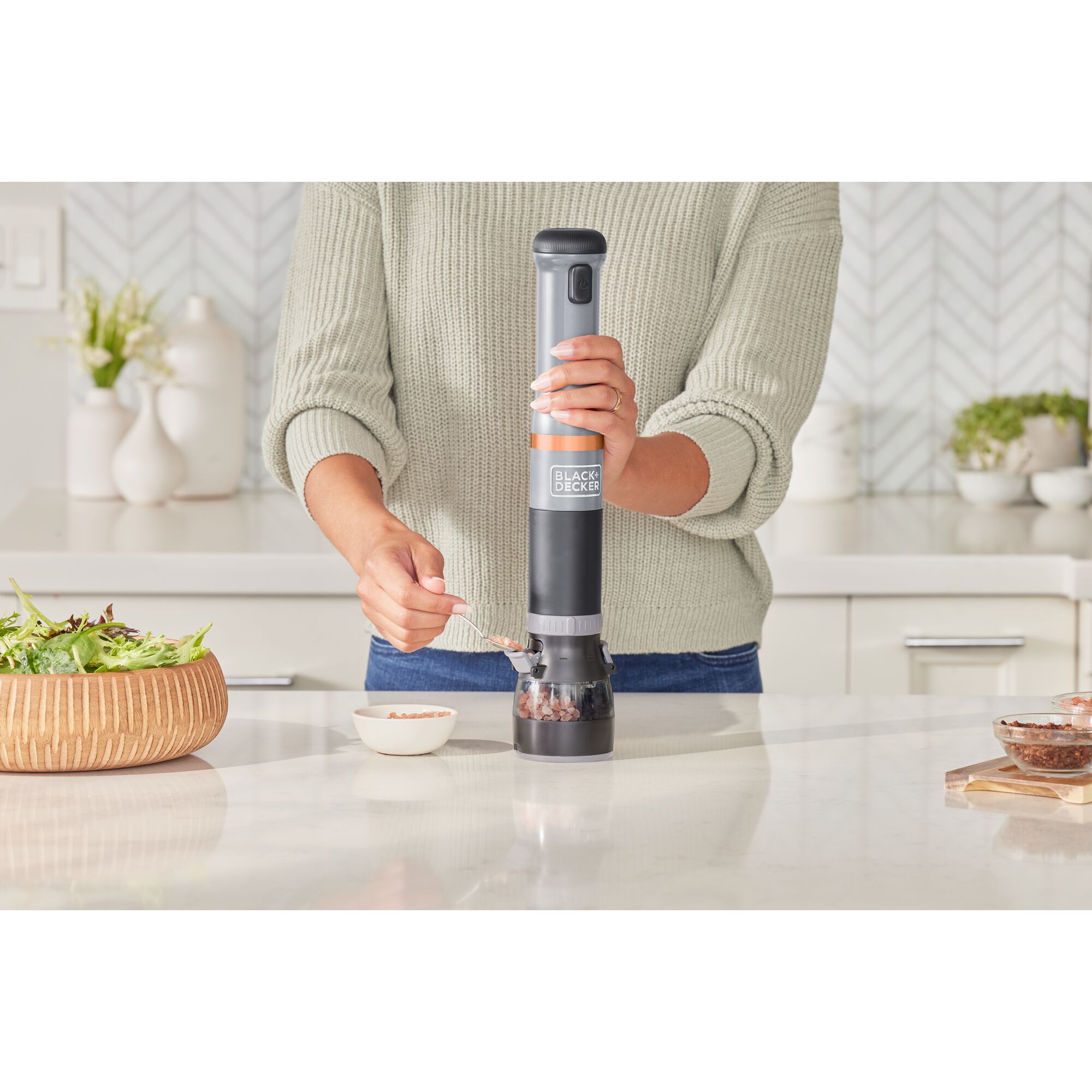 Talent adding salt crystals to the grey BLACK+DECKER kitchen wand spice grinder attachment