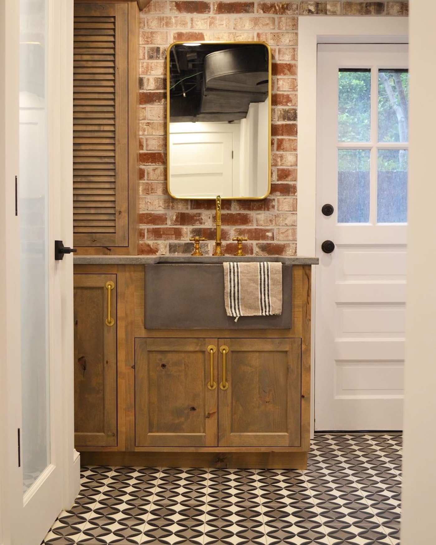 a bathroom with a tiled floor, a brick wall, and a mirror.