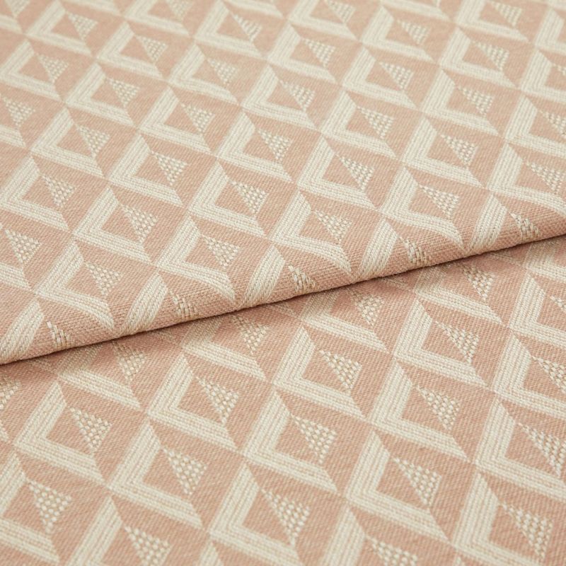 Woven pink geometric jacquard fabric, folded over itself, displaying raised cream triangular diamond pattern; close-up on a flat surface with soft, even studio lighting emphasizing texture.
