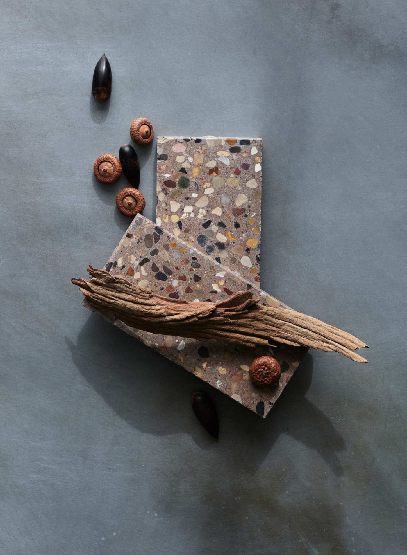 a stack of rectangle terrazzo tiles with bark and acorns on a grey surface.