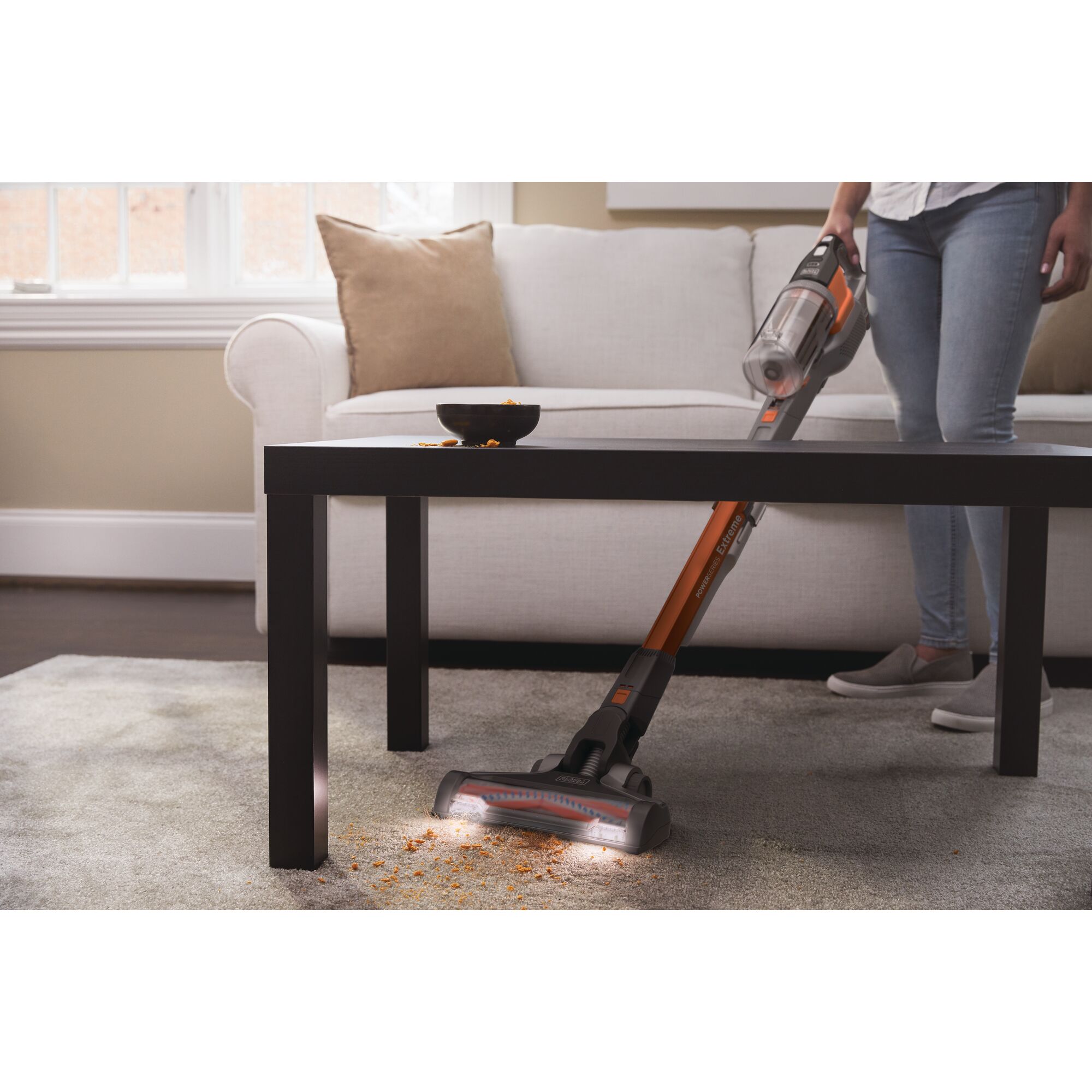 POWER SERIES Extreme cordless stick vacuum cleaner being used by a person to clean carpet under the table.