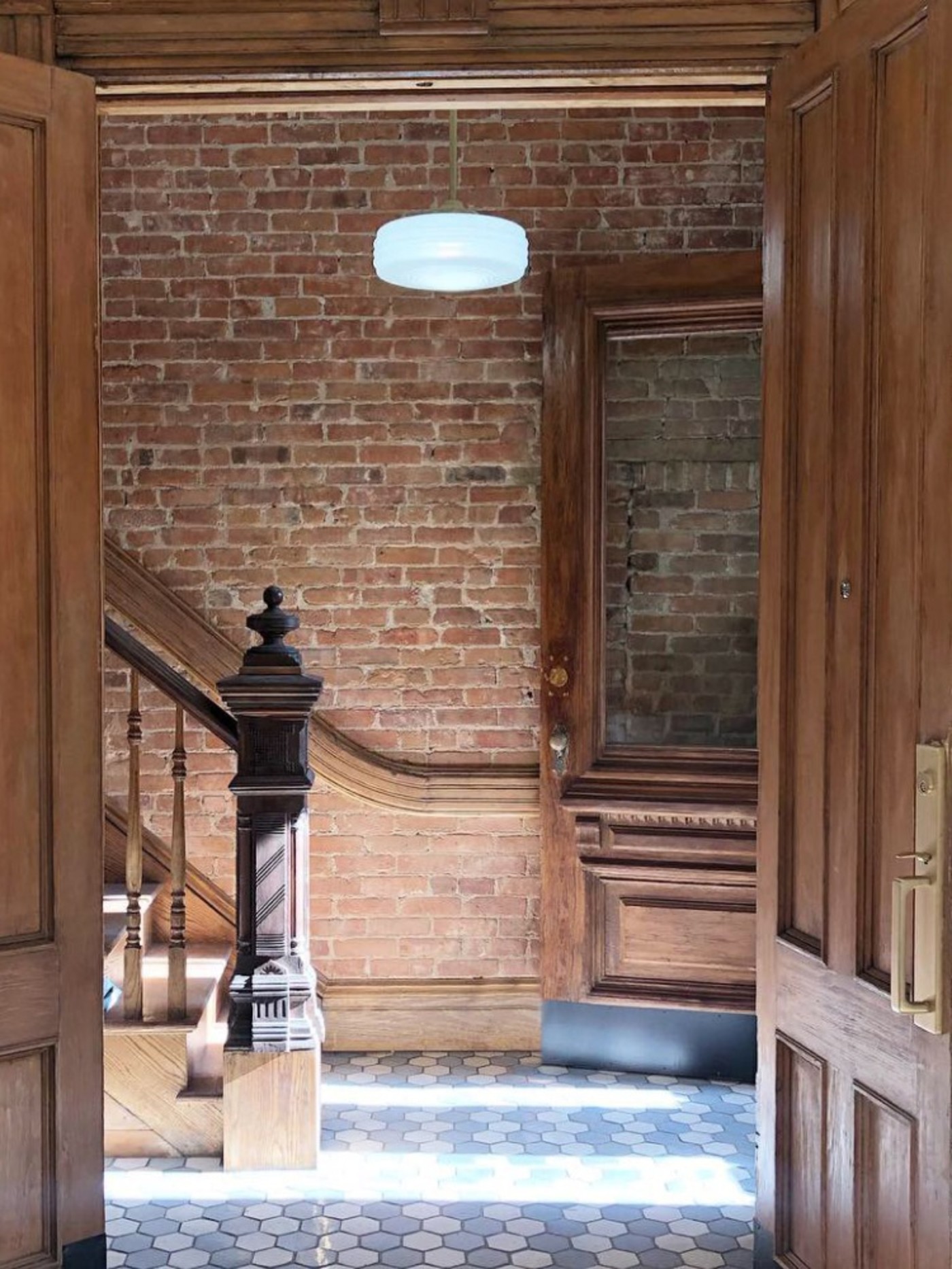 a hallway with a wooden door, a staircase and a brick wall.