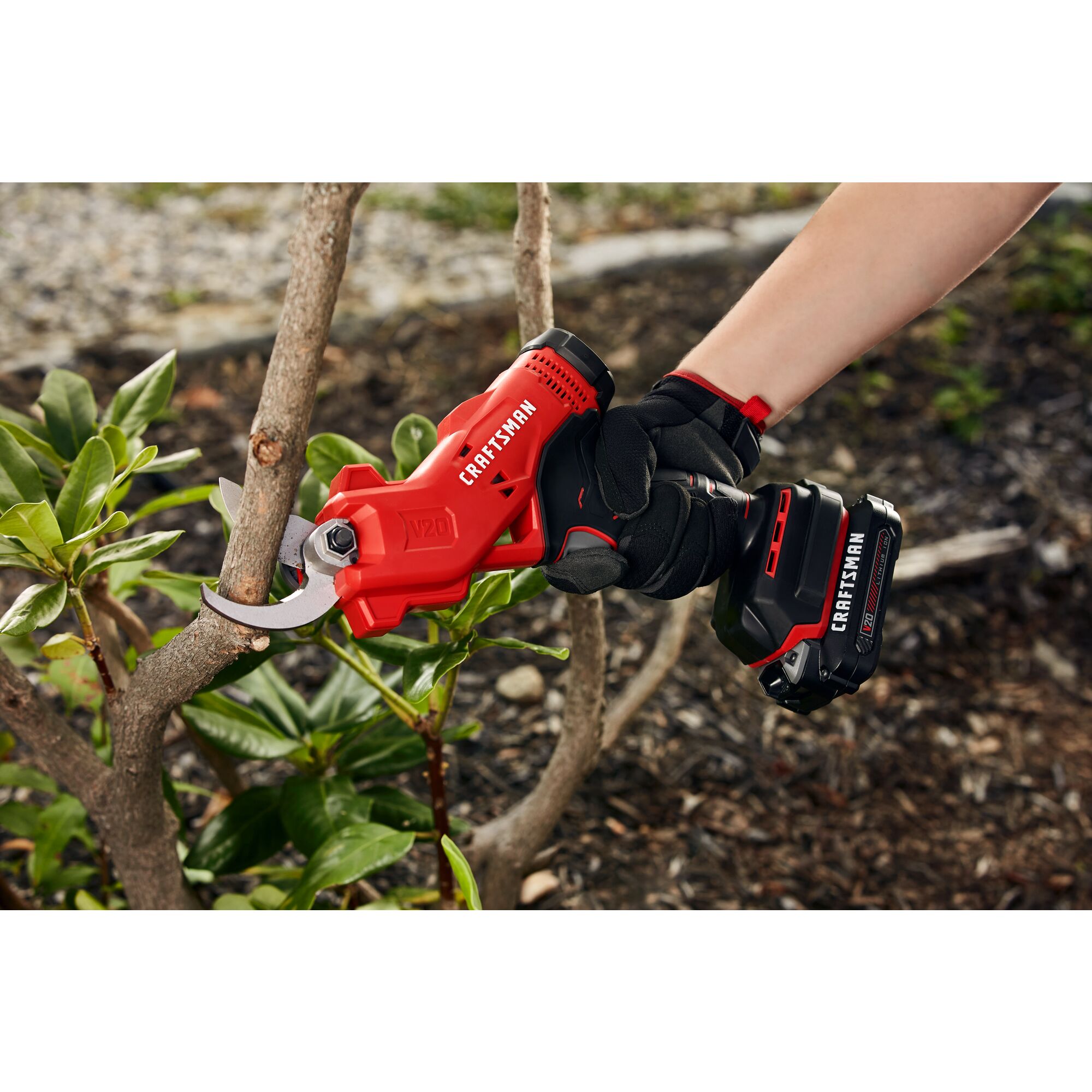 20 volt cordless pruner kit being used by a person to cut a branch outdoors.