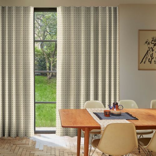 Patterned beige curtains, mostly drawn with a narrow central opening filtering daylight; covering a tall multiâ€‘pane window overlooking a green yard, in a dining room with wooden table and chairs.