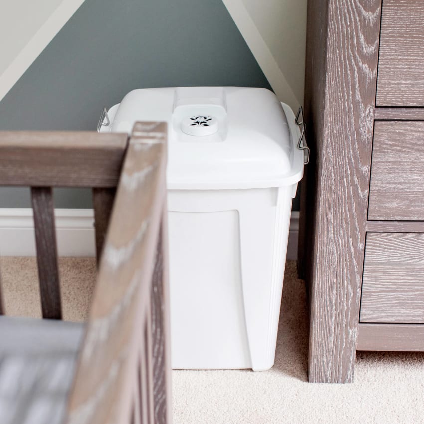 plastic bin for used baby diapers in a baby's room sitting beside the changing table