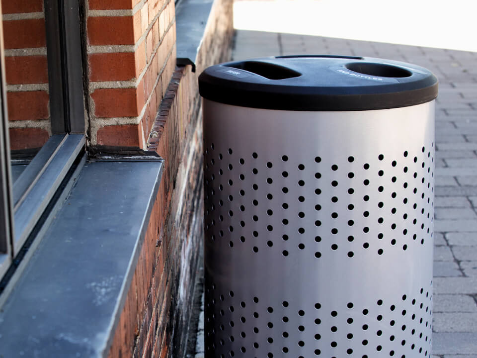 metal triple stream trash and recycling container sitting outside against a red brick wall on a city sidewalk