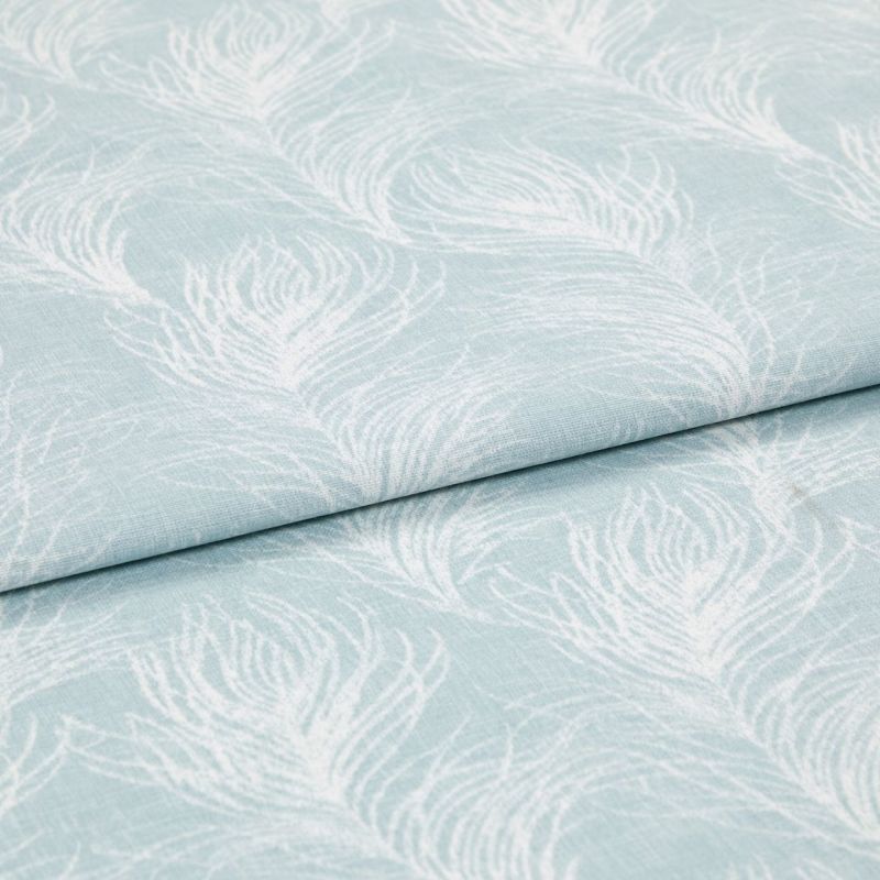 Light blue cotton fabric featuring white peacock-feather motifs, folded once so layers overlap; printed pattern repeats across a soft textile surface in bright, even studio lighting, close-up view.