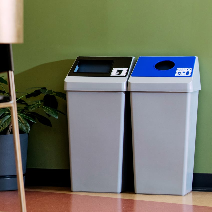 waste and mixed recycling bins in a double station with color coded restrictive openings sitting in a corporate office cafeteria