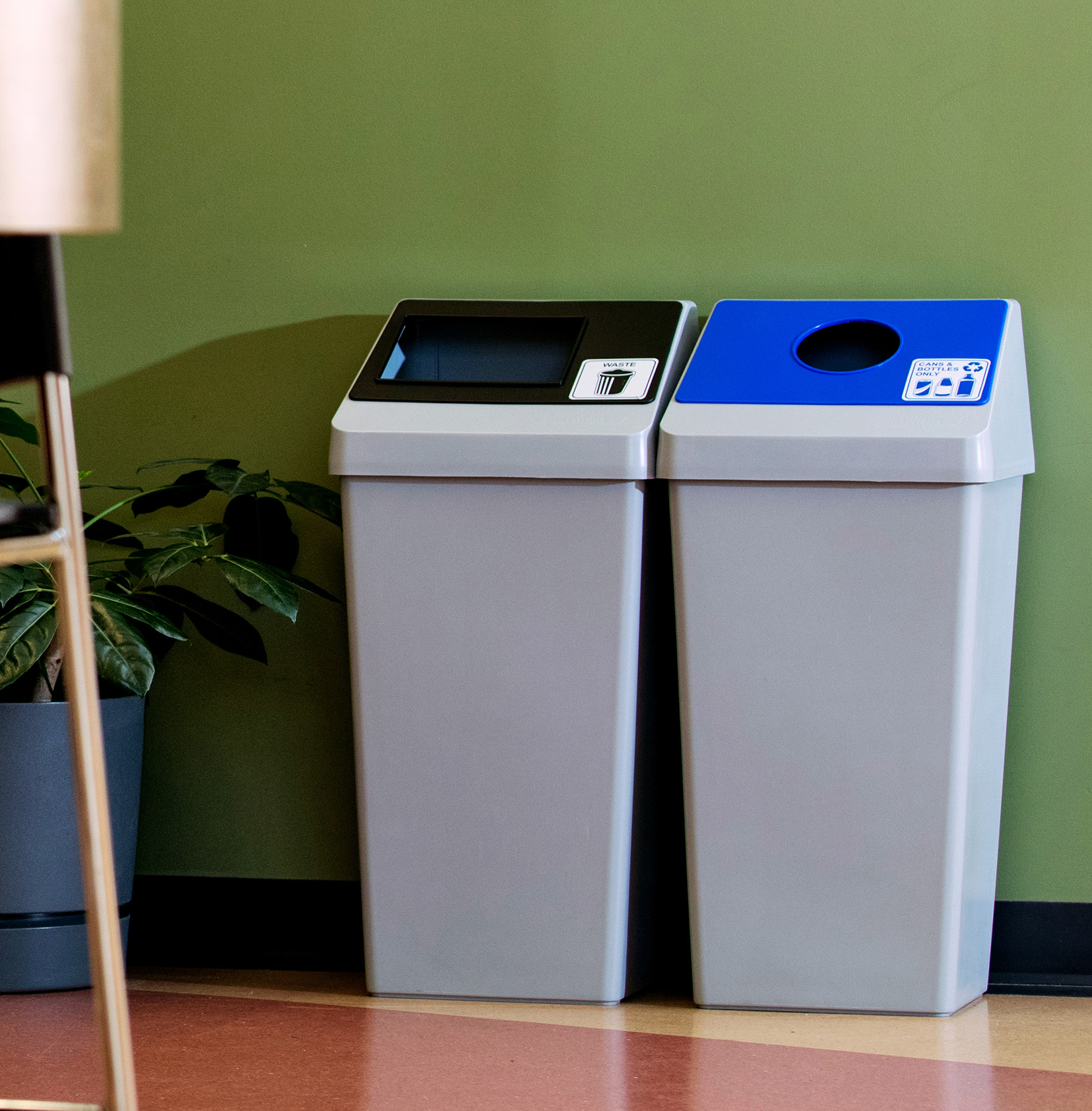 waste and mixed recycling bins in a double station with color coded restrictive openings sitting in a corporate office cafeteria