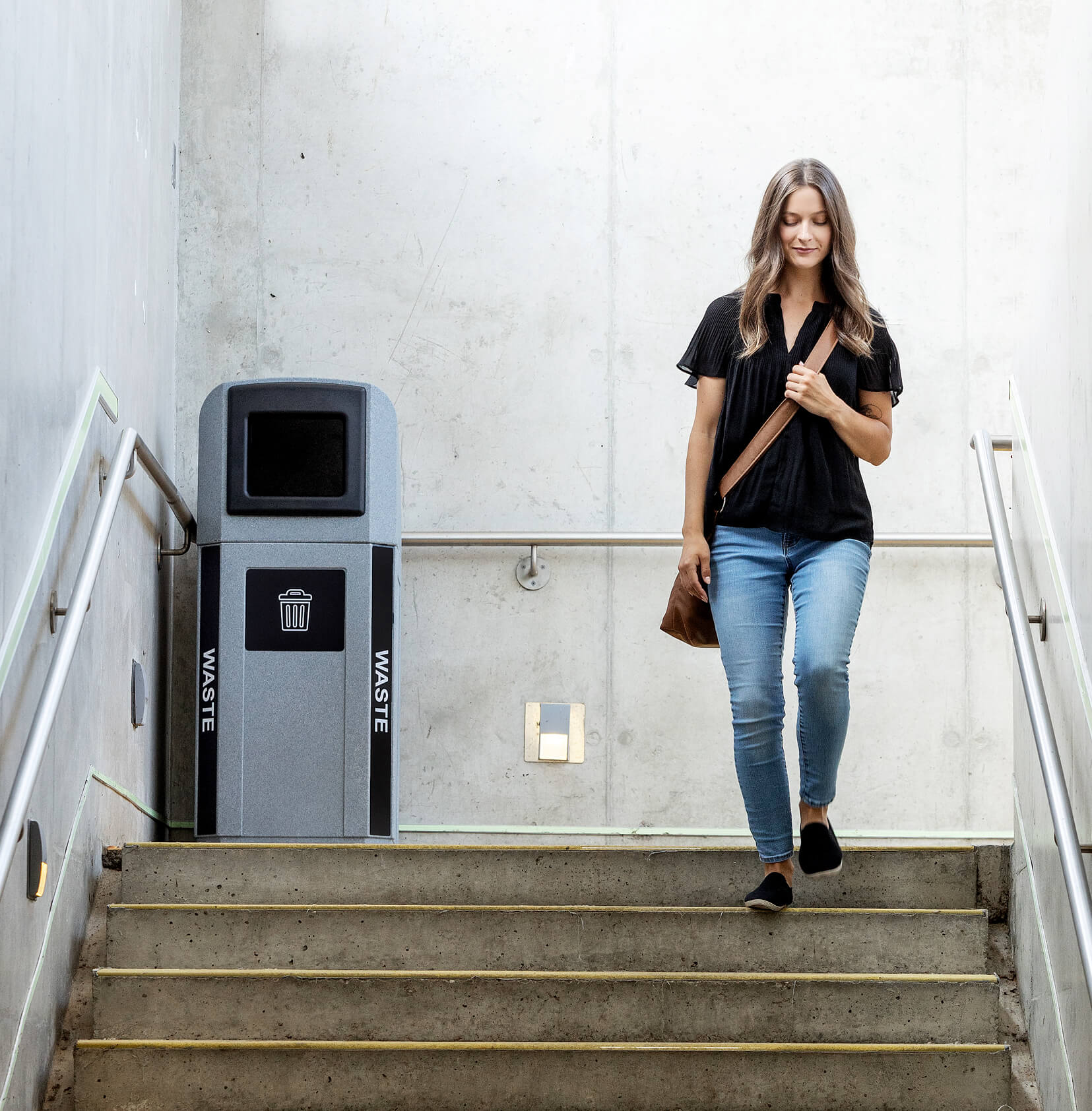 outdoor waste bin with a canopy lid and color coded trim and labels in a busy transit station with a woman walking down the stairs