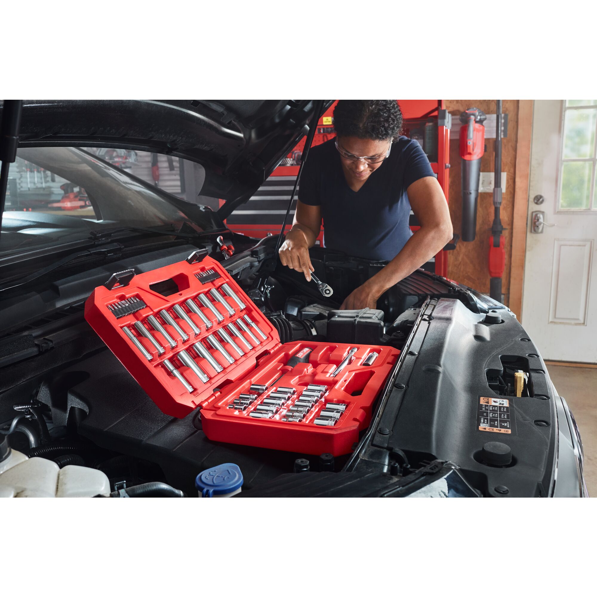 User working under hood of a vehicle with rachet set open nearby 