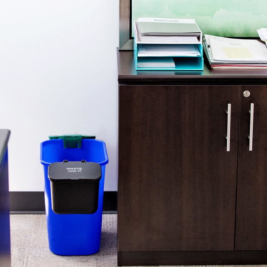 blue recycling bin with two hanging waste and organics collection bins on each side sitting beside a desk in an office