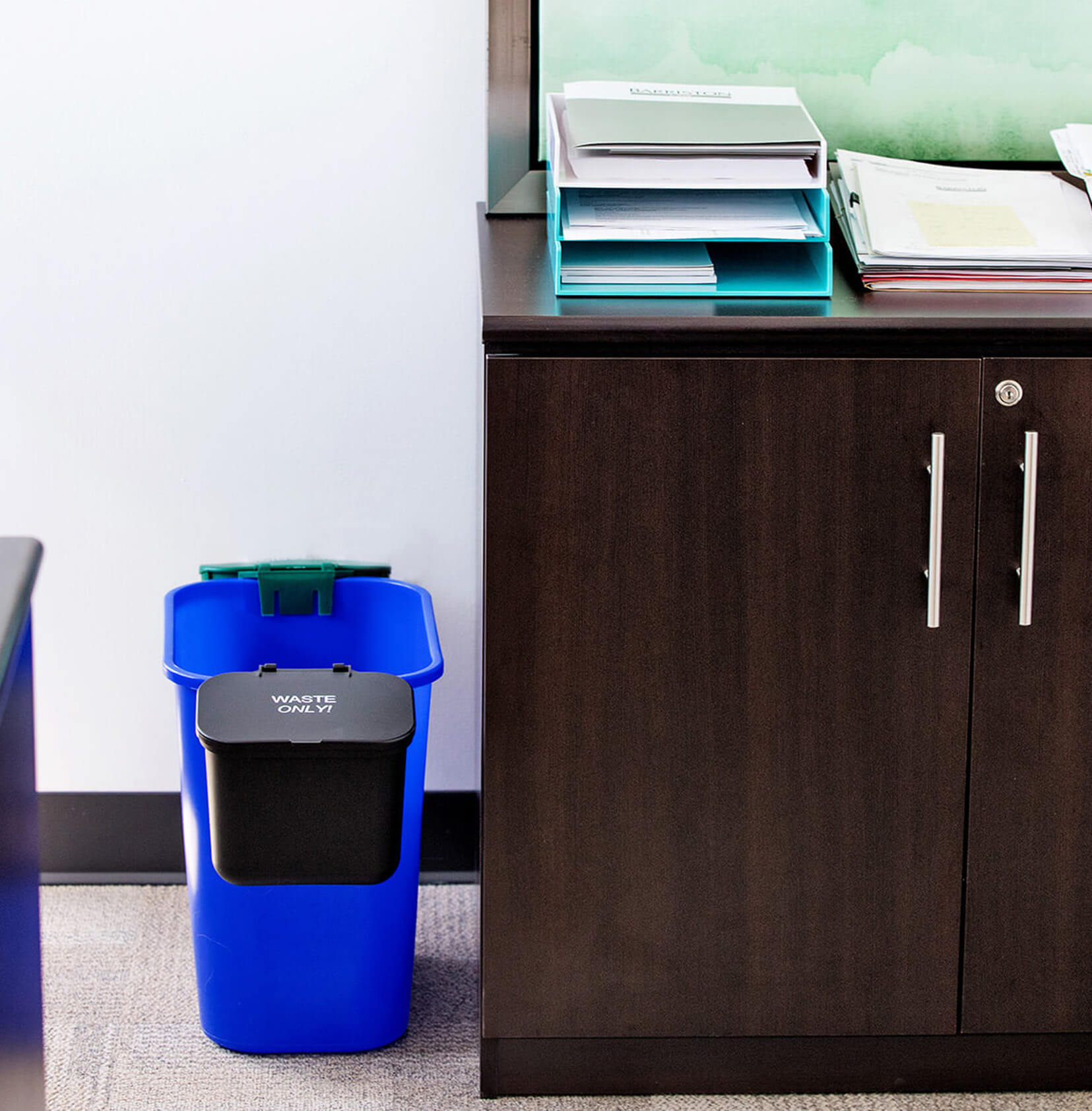 blue recycling bin with two hanging waste and organics collection bins on each side sitting beside a desk in an office