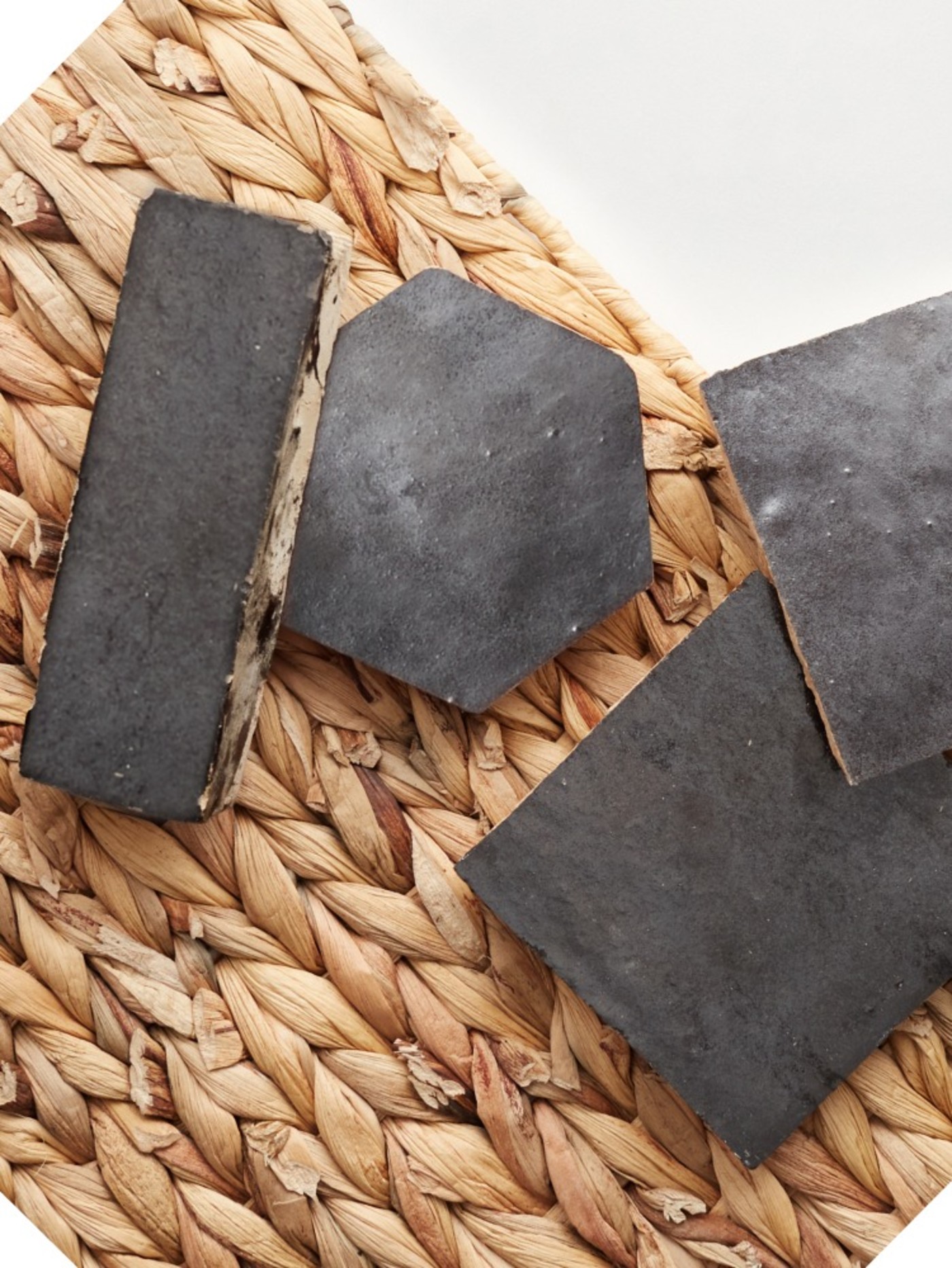 four pieces of black tile on a rattan rug.