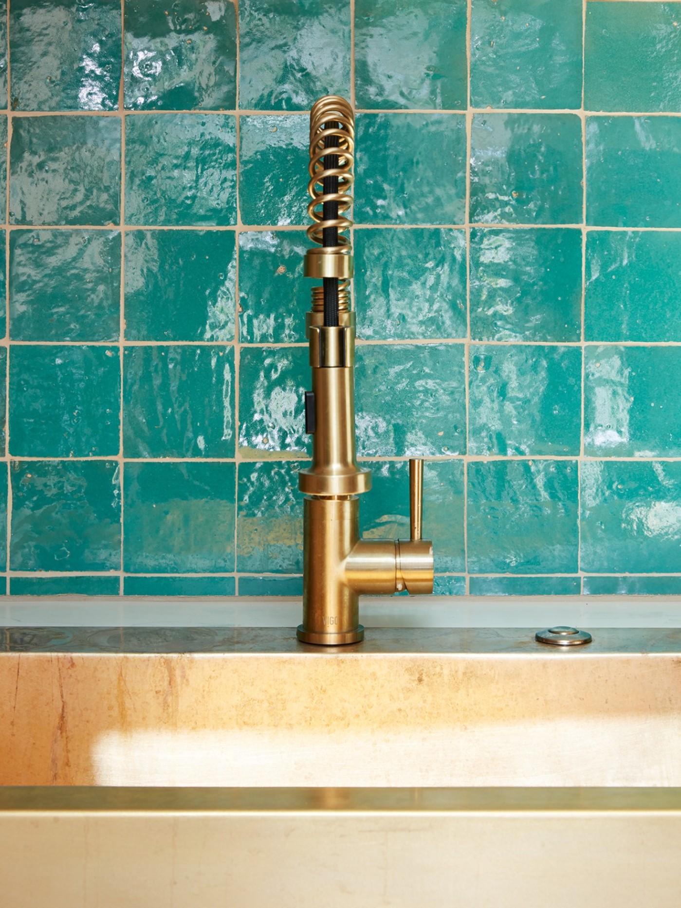 a sink in a bathroom with a green tiled backsplash.