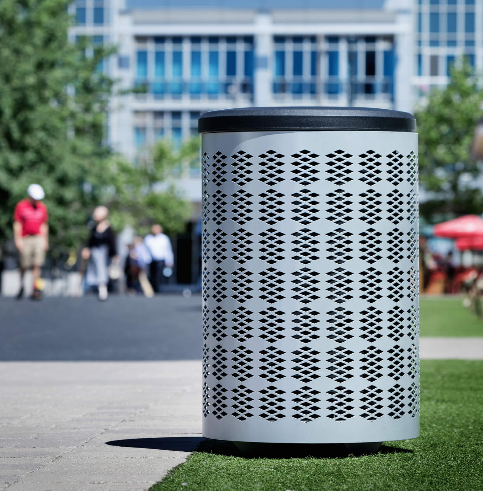 silver metal outdoor waste bin with a durable plastic lid  on a sunny day at a downtown park area