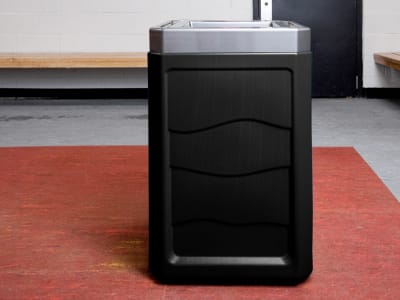 trash bin with a black 100% PCR material body and a brushed pewter lid sitting in a arena change room