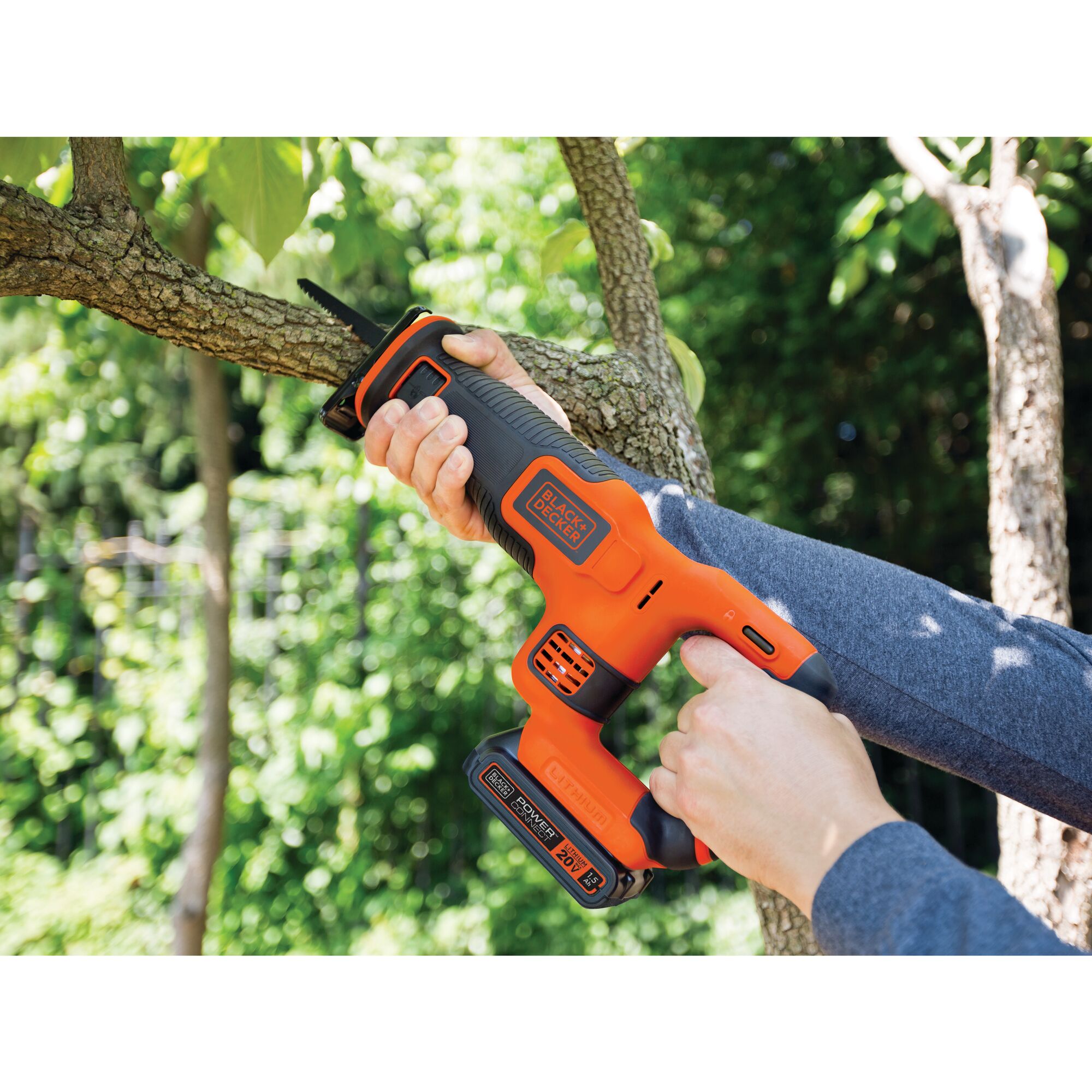 Cordless reciprocating saw being used to saw a branch.