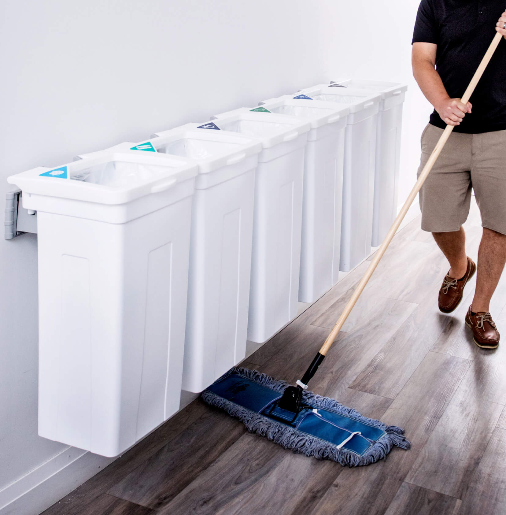 white waste and recycling collection station hanging on a wall with a man sweeping the floor