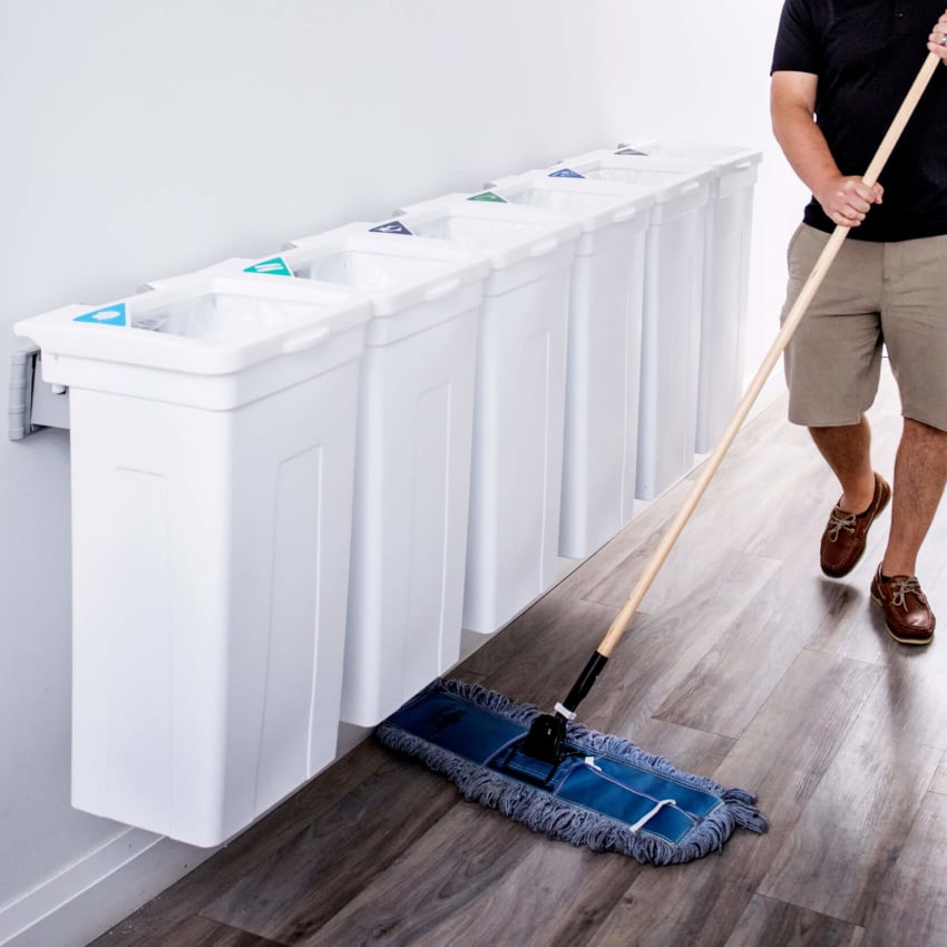 white waste and recycling collection station hanging on a wall with a man sweeping the floor