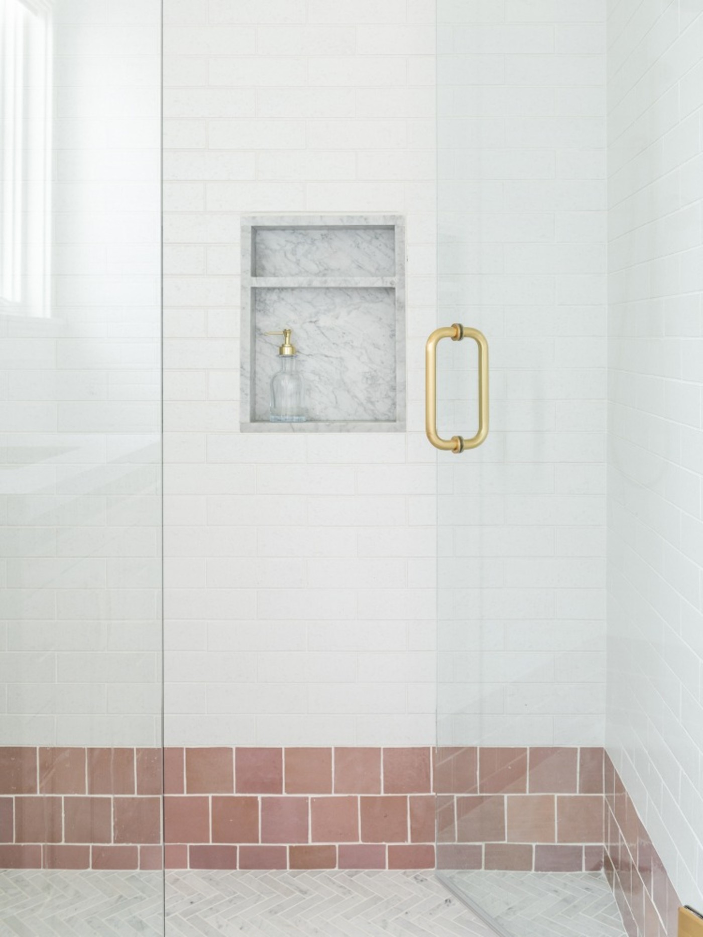 a bathroom with a glass shower door and pink and white tile.