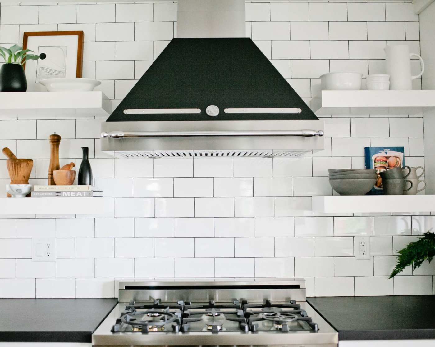 a white tiled kitchen with black counters and white shelves.