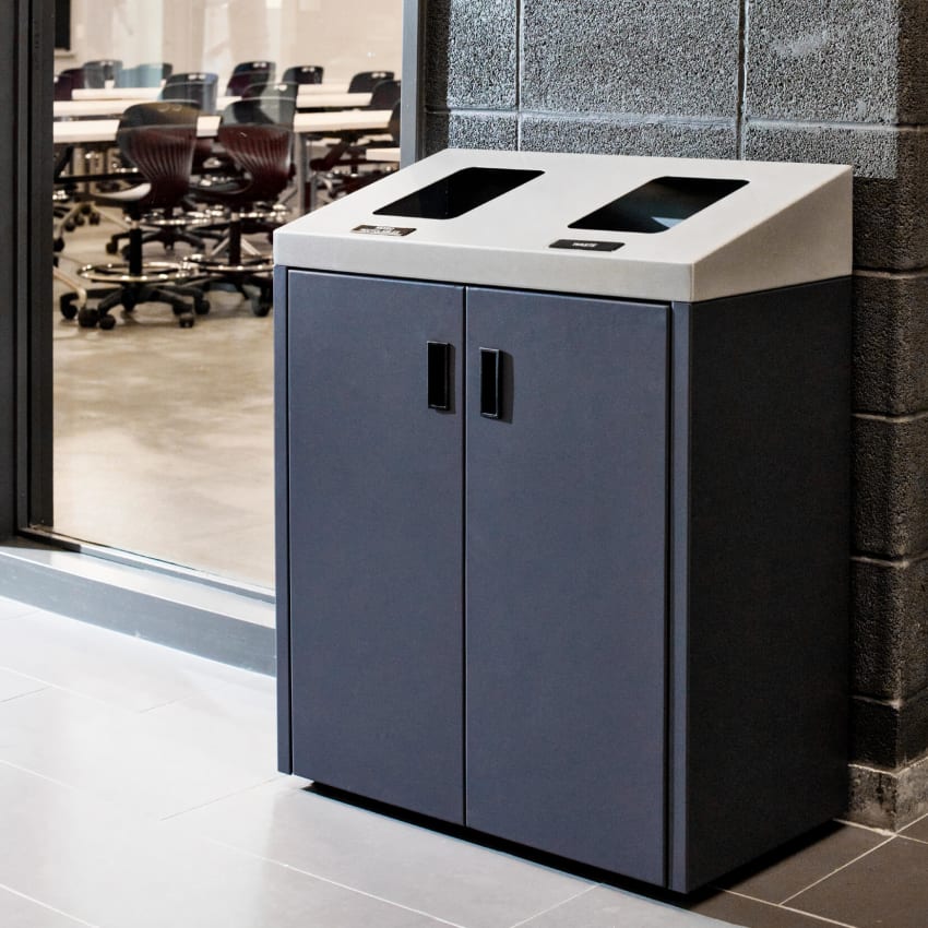 powder coated steel double waste and recyclables bin with a sloped top sitting in the hallway outside a college classroom