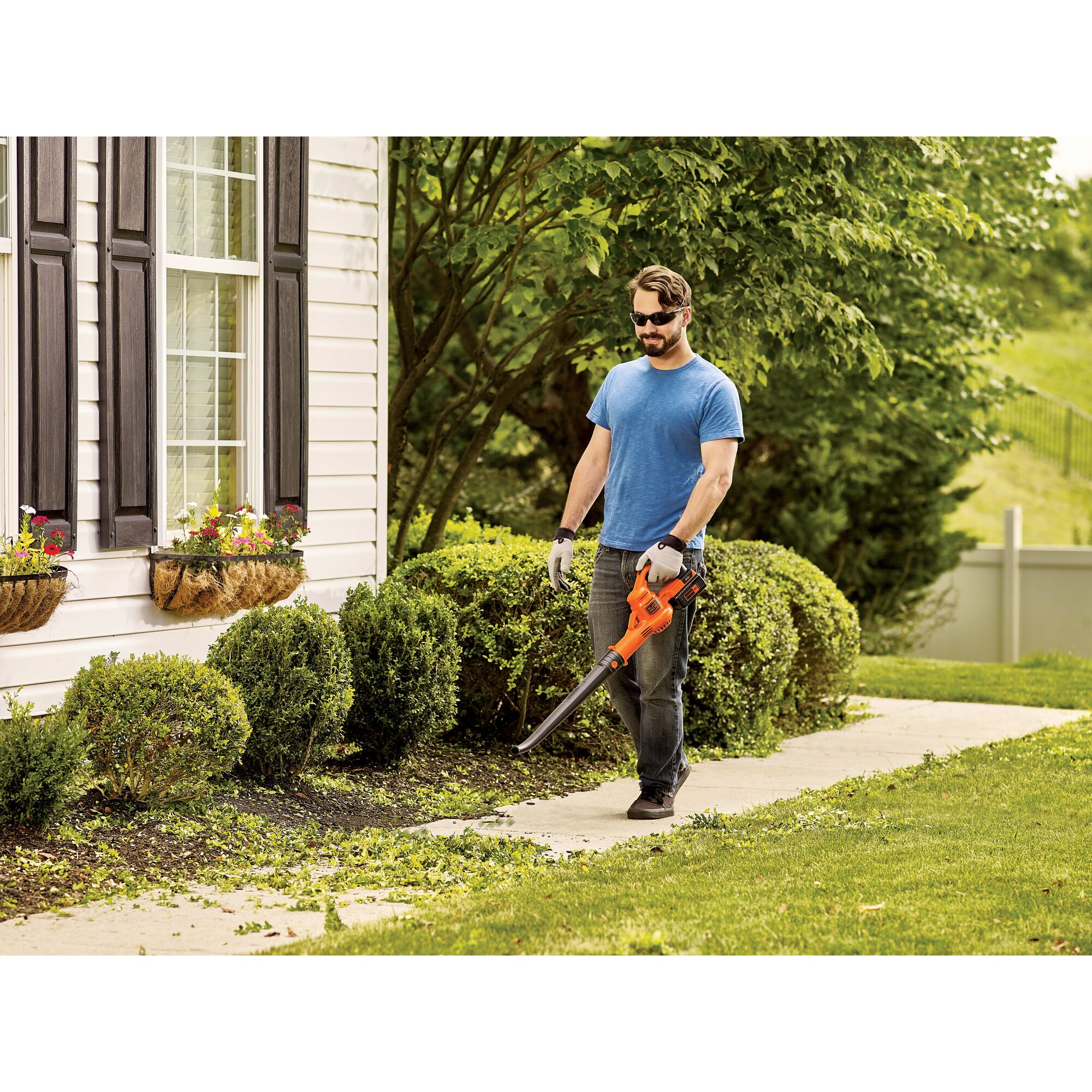 Man using 40V Max Sweeper to blow grass off of a residential walkway.