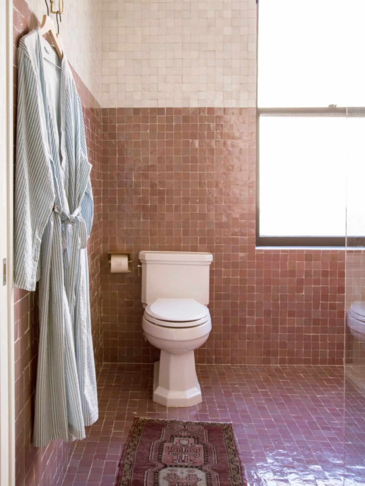 a pink tiled bathroom with a robe and toilet.