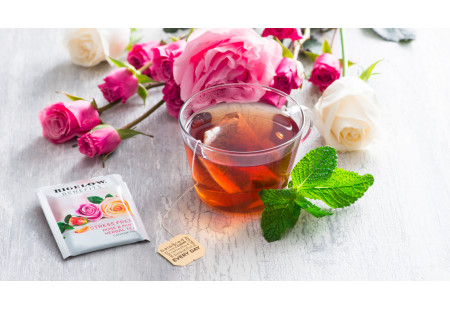 Lifestyle image of a cup of Rose and Mint herbal tea  with tea bag and foil wrap