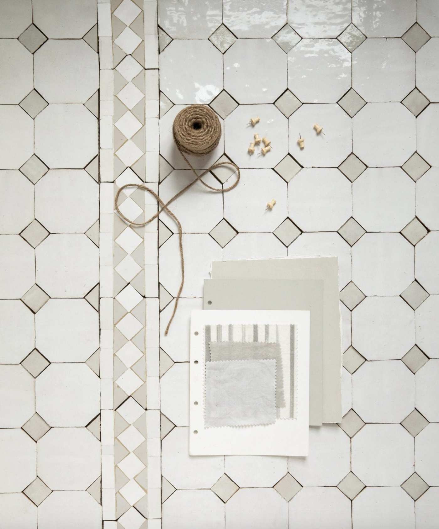 a tiled floor with a white and grey pattern, a roll of twine and sheets of paper.