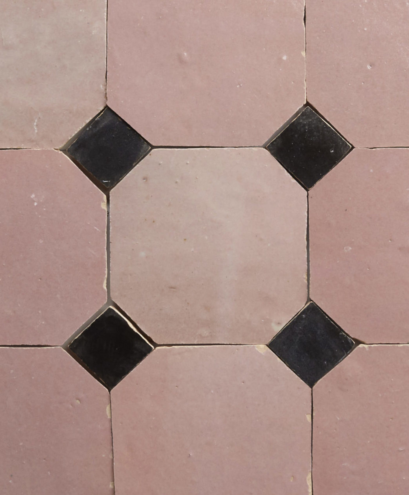 a close up of a pink tile floor with black squares.