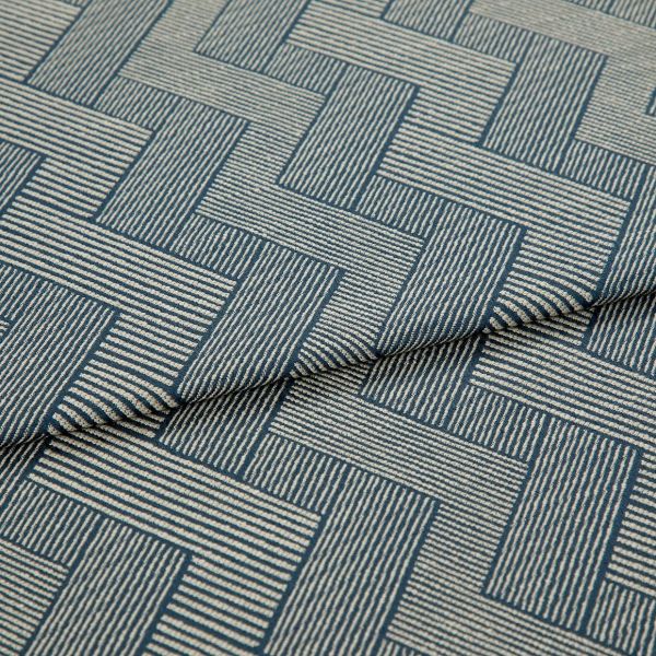 Blue-and-cream woven fabric with interlocking rectangular striped pattern, partially folded and layered, showing raised texture and seam â€” close-up on a flat surface under soft studio lighting.