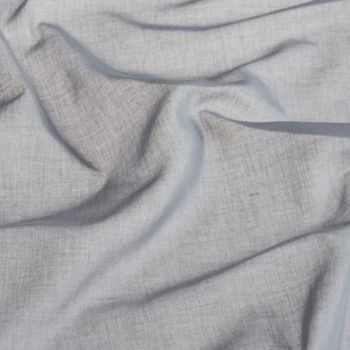 Light-gray woven fabric (linen-like) draped and rumpled into soft folds and creases, lying across a flat surface in diffuse indoor light, showing visible weave texture and subtle shadows.
