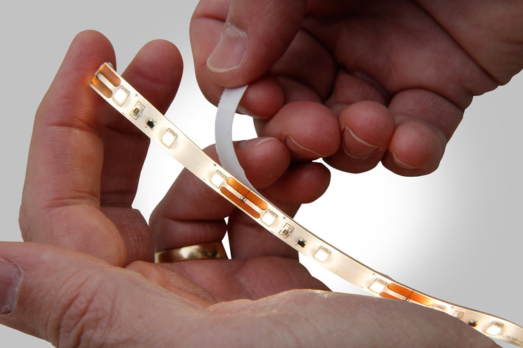 Hands pulling off backing of lit Tetra tape for installation