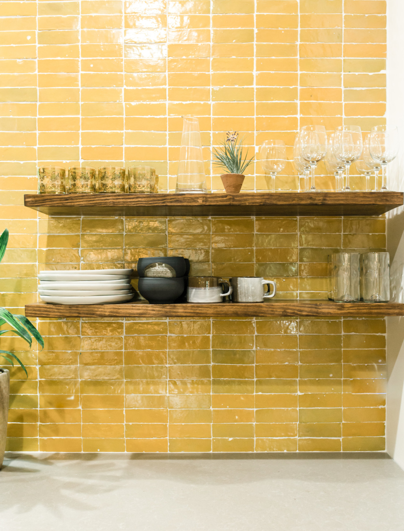 a yellow tiled wall with shelves and a potted plant.