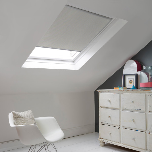 Room with white eaves wall, dark blue-grey wall to right with a shabby chic white drawer unit, a contemporary white chair, white painted floorboards and a skylight blind in pale flint grey.