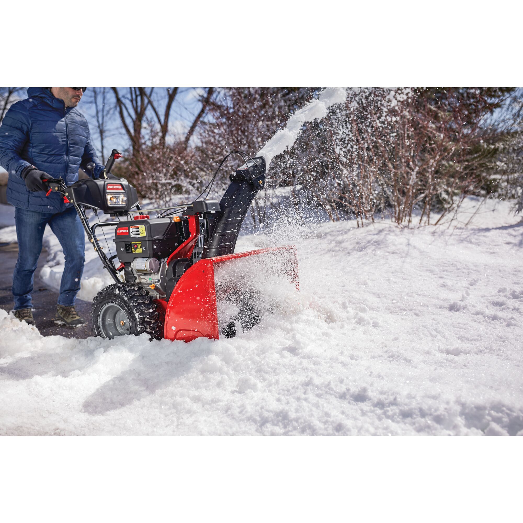 CRAFTSMAN Electric Start 3-Stage Snow Blower blowing the snow off a sidewalk in a yard in side view in blue jacket