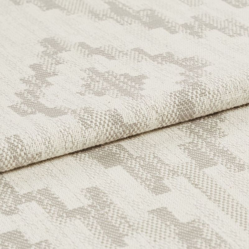 Woven upholstery fabric with light beige geometric motif, folded over once showing textured weave; close-up studio shot with neutral lighting emphasizing fibers and subtle pattern.